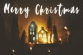 Merry Christmas text sign. Season`s greeting card. New Year. Christmas little houses with lights and trees in christmas evening Royalty Free Stock Photo