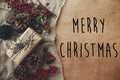 Merry Christmas text sign on stylish rustic christmas gift box with fir branches, red berries, pine cones on rustic wood. Royalty Free Stock Photo