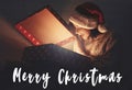 Merry Christmas  text sign on stylish surprised girl in santa hat opening christmas gift box with magic light in dark room. Happy Royalty Free Stock Photo