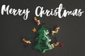 Merry Christmas text on Stylish little christmas tree flat lay with sparkling gold confetti on black paper. Season`s greeting car Royalty Free Stock Photo