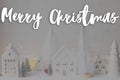 Merry Christmas text on stylish little white houses and trees, snowy christmas miniature village with golden lights. Happy Royalty Free Stock Photo