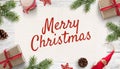Merry Christmas text on white paper surrounded by Christmas decorations and gifts on white wooden surface Royalty Free Stock Photo