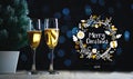 Merry Christmas Typography Art. Two Glasses of Champagne and Small Christmas Tree Dark Glow Lights Background. Royalty Free Stock Photo