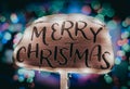 Merry Christmas wooden sign illuminated with holiday lights against a backdrop of Christmas trees adorned with festive lights Royalty Free Stock Photo