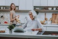 Merry female is watching her mother with notebook in kitchen Royalty Free Stock Photo