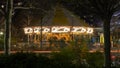 A merry go round at night glowing with lights, through the trees from across a street