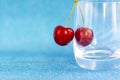 Merry. Red cherries hang on transparent glass. A ripe berry in a glass on a blue background. Royalty Free Stock Photo