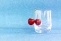 Merry. Red cherries hang on transparent glass. A ripe berry in a glass on a blue background. Royalty Free Stock Photo