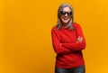 Merry senior middle-aged woman wearing sunglasses standing with arms crossed isolated on yellow. Studio shot of cheerful