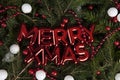 merry xmas written on a glossy red plastic wall decoration placed on a pile of fir branches