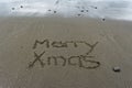 Merry Xmas written in the sand with wet sand behind