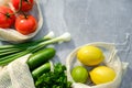 Mesh produce bags with fresh vegetables and fruits on stone concrete table. Top view tomatoes, cucumbers, onion, parsley, lemon Royalty Free Stock Photo