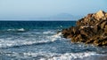 Mesmerizing landscape with the sea in which waves rage and crash against stone breakwaters, with mountains visible in