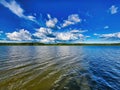 A mesmerizing scenery of a blue sea. Clear and very bright blue sky with calm river water. Green shore. A small white ship on a Royalty Free Stock Photo