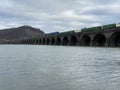 Mesmerizing shot of freight train passing the arch bridge over the river under a cloudy sky Royalty Free Stock Photo