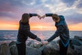 Mesmerizing shot of a loving couple making a heart shape with their arms on the sunset background