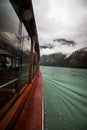 Mesmerizing vertical shot of a mountain at the lake covered in mist, shot from the ship window Royalty Free Stock Photo