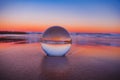Mesmerizing view of a clear crystal ball placed on the sand near the beach during the sunset Royalty Free Stock Photo