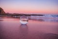 Mesmerizing view of a clear crystal ball placed on the sand near the beach during the sunset Royalty Free Stock Photo