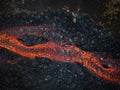 Red hot lava flow streaming over black volcanic rocks, aerial directly above