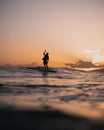 Mesmerizing view of a silhouetted surfer on the sea waves under a cloudy orange sky at sunset Royalty Free Stock Photo