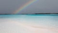 Mesmerizing view of a tropical beach and shallow water, with a rainbow and cloudy sky over the sea Royalty Free Stock Photo