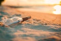 Message in the bottle washed ashore against the sunset. Bottle with a message