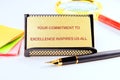 A message about commitment to excellence sits on a desk alongside colorful sticky notes, a magnifying glass, and a Royalty Free Stock Photo