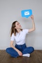 A beautiful caucasian girl sits on the floor and holds a icon messages in messenger above her head