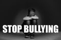 Message STOP BULLYING and sad little boy sitting on floor near dark wall