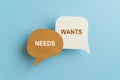 Message WANTS vs NEEDS on real brown and white speech bubble paper cut with blue background, for choice conceptual image Royalty Free Stock Photo