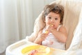 Messy baby girl eating cake. Lovely infant girl holding a spoon, enjoying eating cake