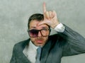 Messy businessman in suit and tie sad and ashamed in weird broken nerdy glasses doing loser sign with hand and fingers on his Royalty Free Stock Photo