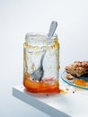 Nearly empty jar of homemade apricot preserves with spoon beside plate with scone