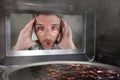 Messy and funny dummy man in the kitchen looking through microwave or oven pizza burning overcooked making a mess of home cook in Royalty Free Stock Photo