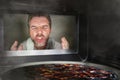 Messy and funny dummy man in the kitchen looking through microwave or oven pizza burning overcooked making a mess of home cook in Royalty Free Stock Photo