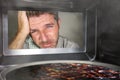 Messy and funny dummy man in the kitchen looking through microwave or oven pizza burning overcooked making a mess of home cook in Royalty Free Stock Photo