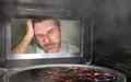 Messy and funny dummy man in the kitchen looking through microwave or oven pizza burning overcooked making a mess of home cook in Royalty Free Stock Photo