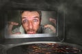 Messy and funny dummy man in the kitchen looking through microwave or oven pizza burning overcooked making a mess of home cook in Royalty Free Stock Photo