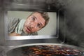 Messy and funny dummy man in the kitchen looking through microwave or oven pizza burning overcooked making a mess of home cook in Royalty Free Stock Photo