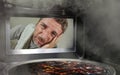 Messy and funny dummy man in the kitchen looking through microwave or oven pizza burning overcooked making a mess of home cook in Royalty Free Stock Photo