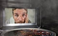 Messy and funny dummy man in the kitchen looking through microwave or oven pizza burning overcooked making a mess of home cook in Royalty Free Stock Photo