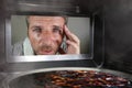 Messy and funny dummy man in the kitchen looking through microwave or oven pizza burning overcooked making a mess of home cook in Royalty Free Stock Photo