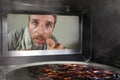 Messy and funny dummy man in the kitchen looking through microwave or oven pizza burning overcooked making a mess of home cook in Royalty Free Stock Photo