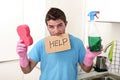 Messy man in stress in washing gloves holding sponge and detergent spray bottle asking for help Royalty Free Stock Photo