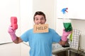 Messy man in stress in washing gloves holding sponge and detergent spray bottle asking for help