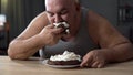 Messy obese man greedily eating cake with whipped cream, addiction to sweets Royalty Free Stock Photo