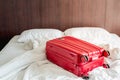 Messy and unmade white traveller`s hotel bed at hotel room with red luggage Royalty Free Stock Photo