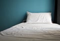 Messy white bed and one pillow , light blue wall