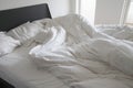 Messy white bedding sheets and pillows with wrinkles on bed in a white bedroom - stock